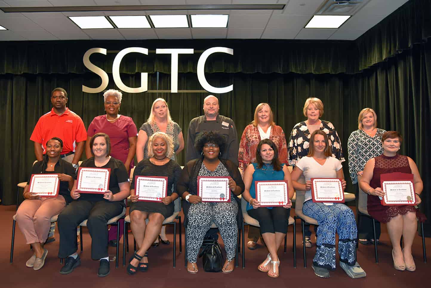 Student of Excellence nominees sit in chairs holding certificates in front of their nominating instructors. Seated left to right: : SGTC Student of Excellence nominees Lashanda Bobbs, Francis Gill, Anaiah Kirkland, Tiara Reese, Melisa Flakes, Shannon Cranford and Sheri Ariail. Standing left to right: Nominating Instructors Xavier Jackson, Dorothea Lusane-Mckenzie, Teresa McCook, Ricky Watzlowick, Jaye Cripe, Lynn Lightner and Christine Rundle.