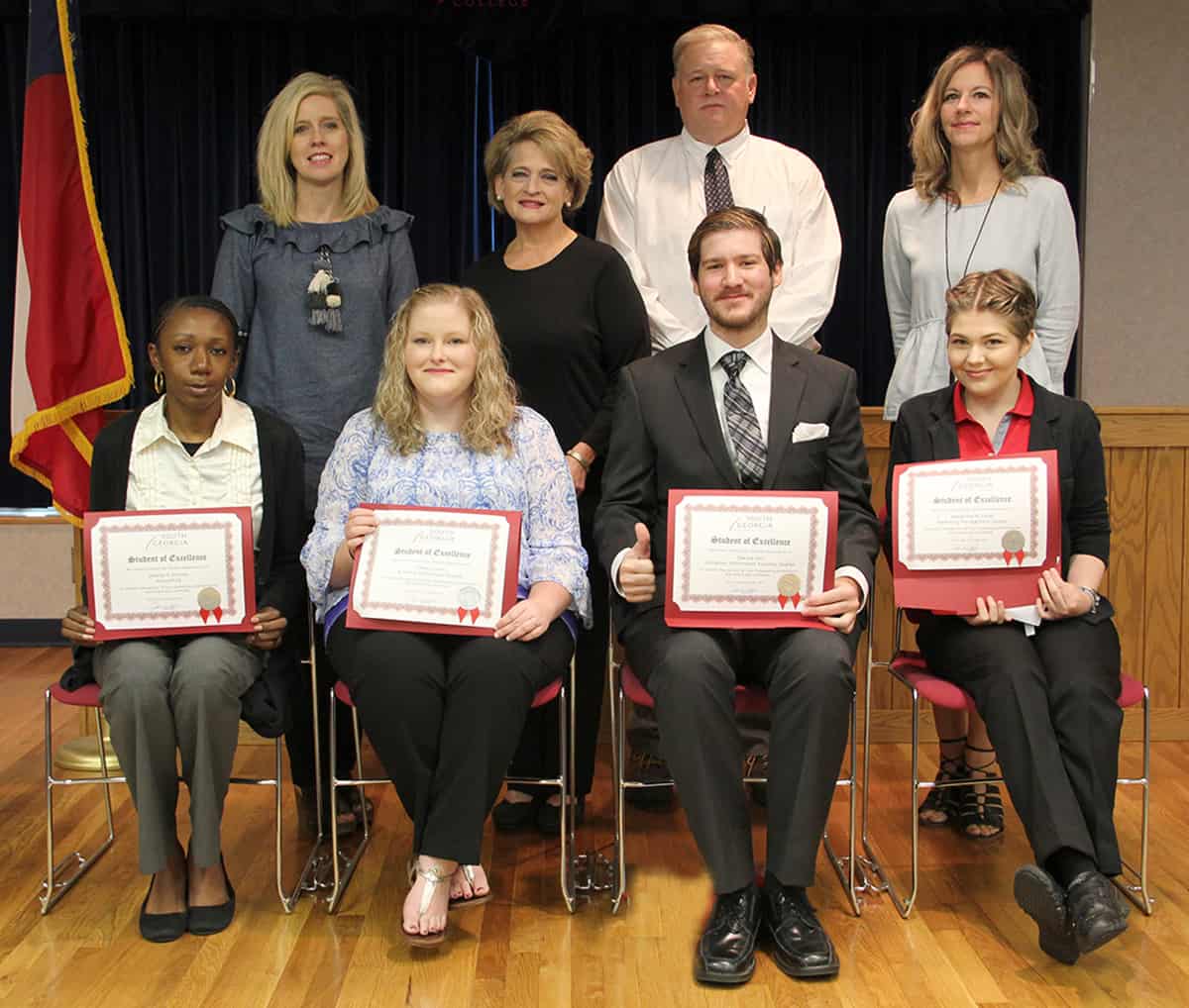 Student of Excellence nominees sit in chairs in front of their nominating instructors. Seated from left to right are: Desiray Kenney, Callie Collier, Dakota Hall, and Alexandra Joiner. Standing left to right: Teresa Jolly, Karen Bloodworth, Randy Greene and Lisa Penton.