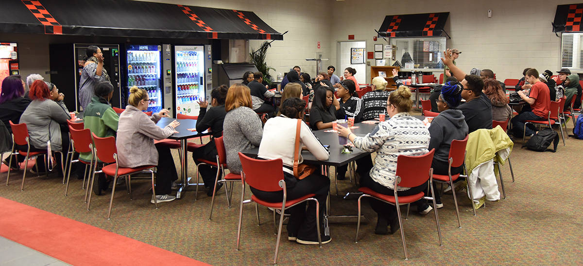 Raven Payne, an SGTC instructor, stands in front of and is talking to four large tables of students.