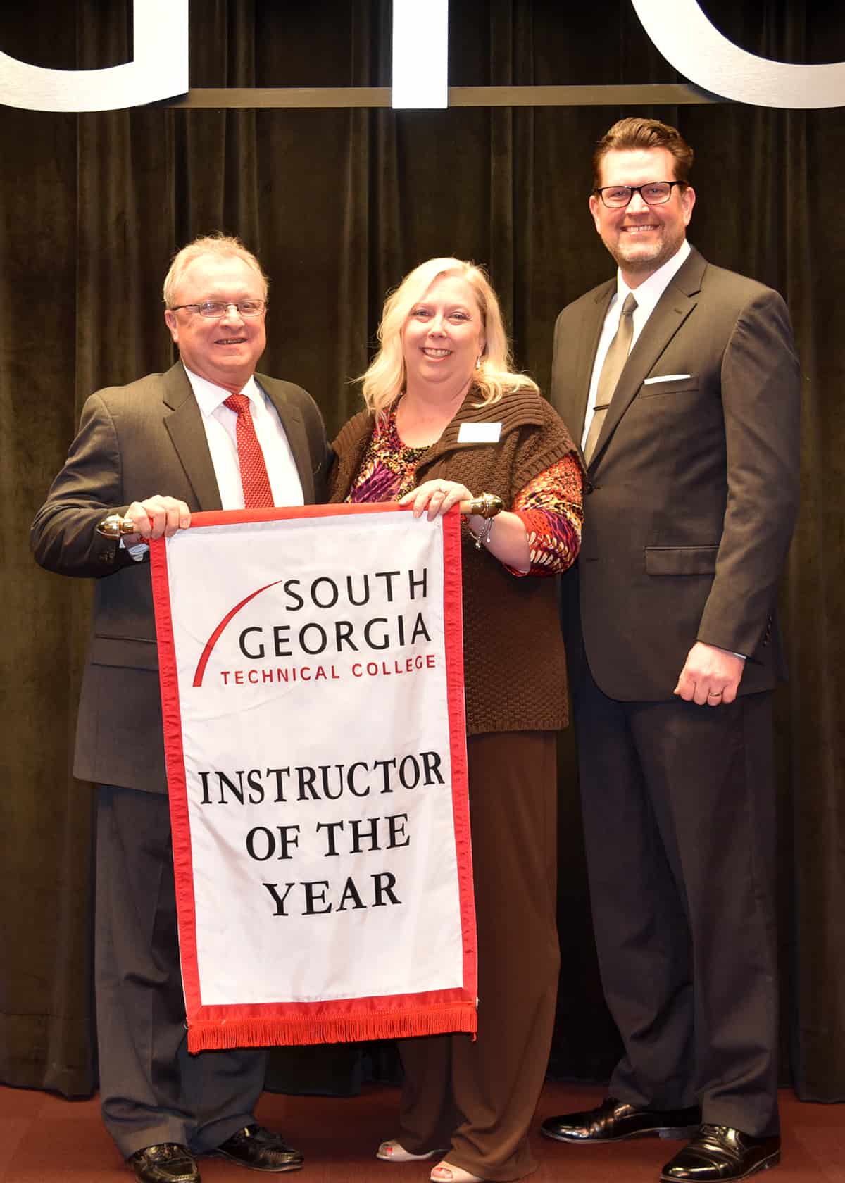 SGTC President Dr. John Watford (right) and 2017 Rick Perkins award winner Charles Christmas (left) pass the award banner off to 2018 Instructor of the Year winner Teresa McCook (middle). 