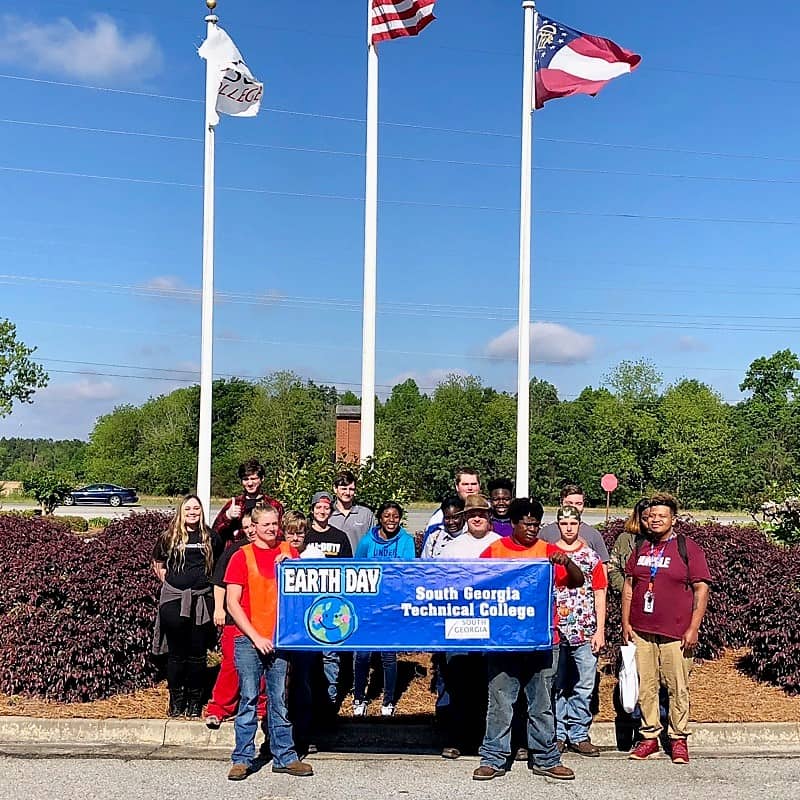 A group of students stand in front of three flag poles.