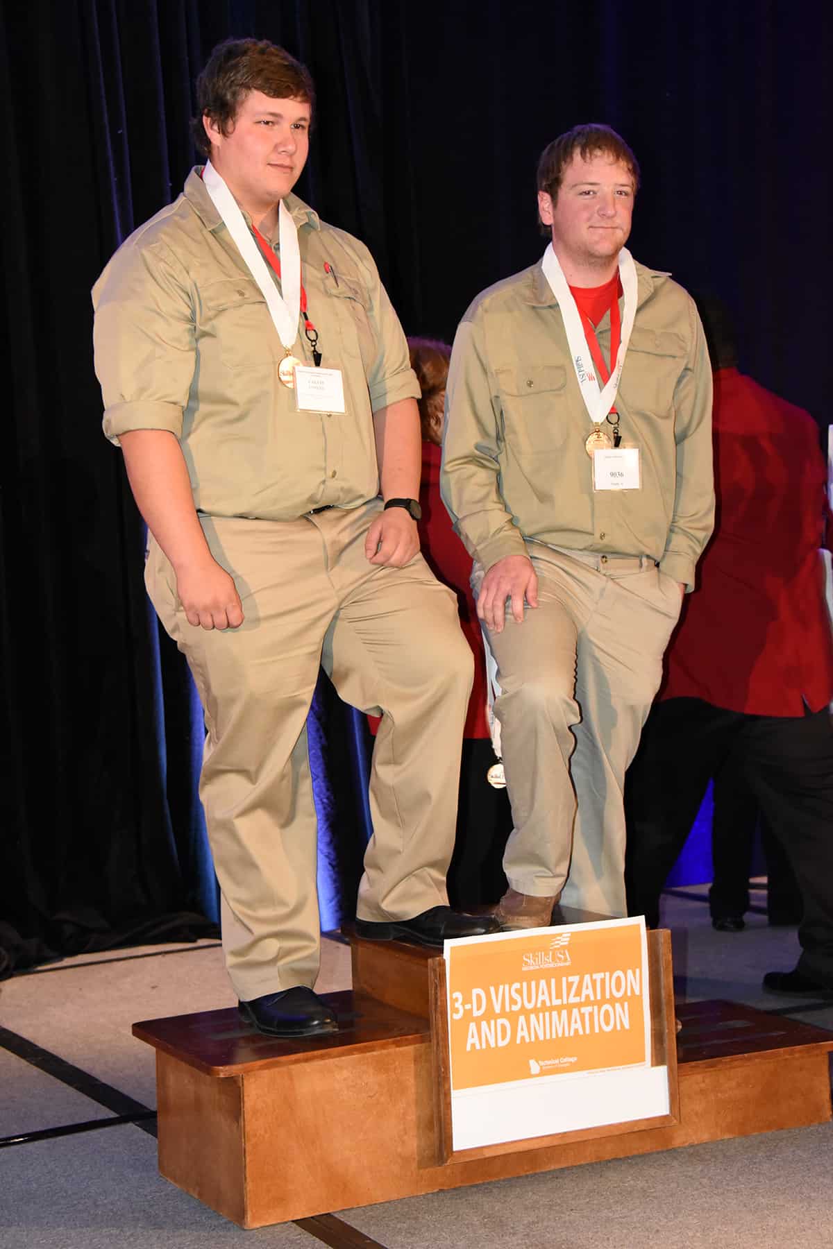 Two males stand on a three tiered podium.