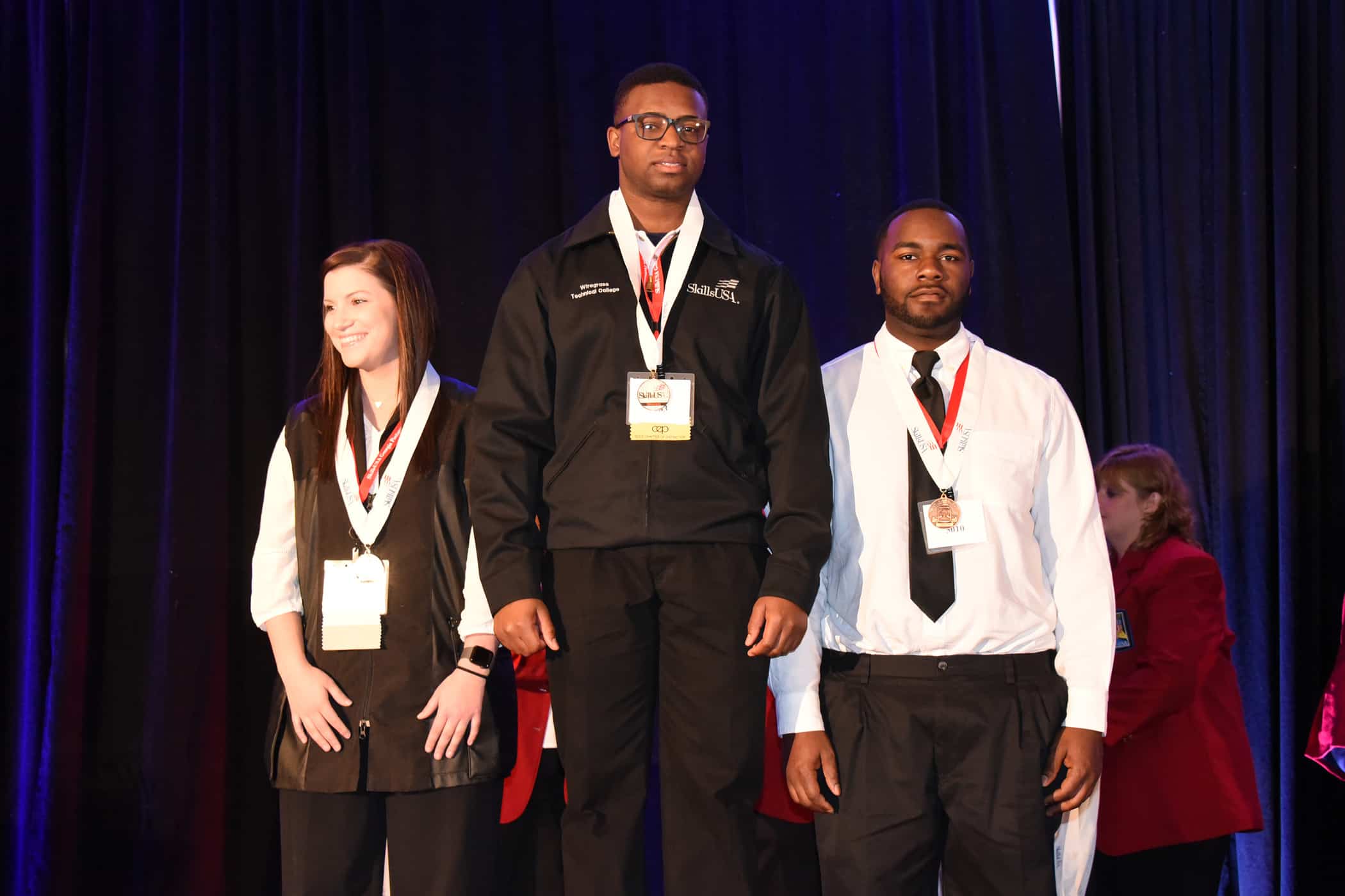 A female and two males stand on a podium.