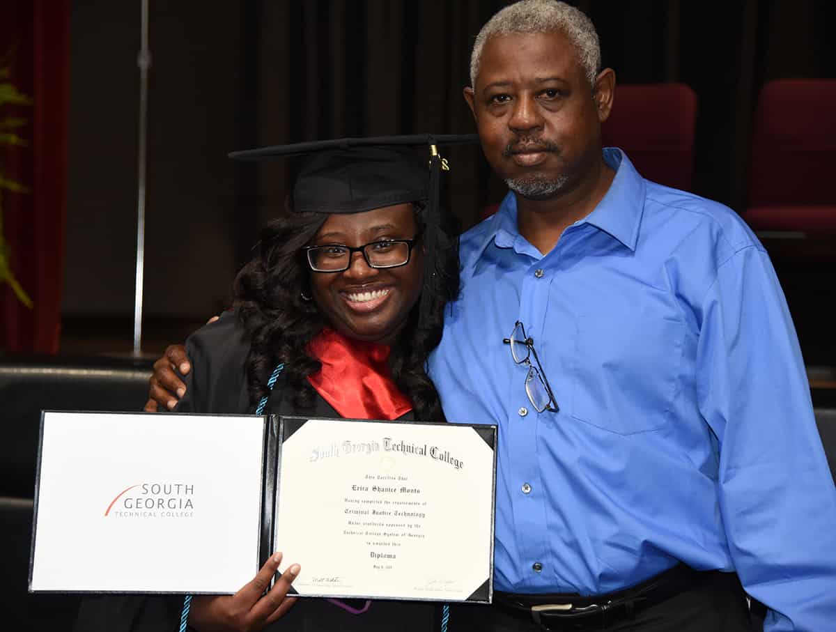 A smiling girl holds her diploma and hugs a man.