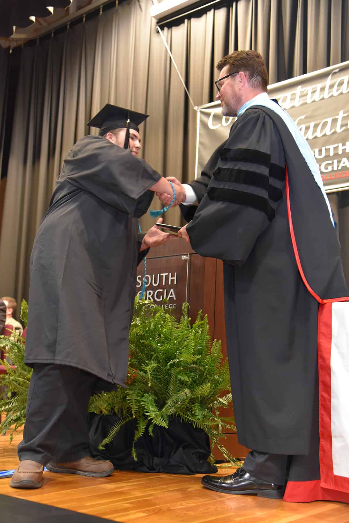 A student wearing a black graduation cap and gown accepts a diploma from a man.