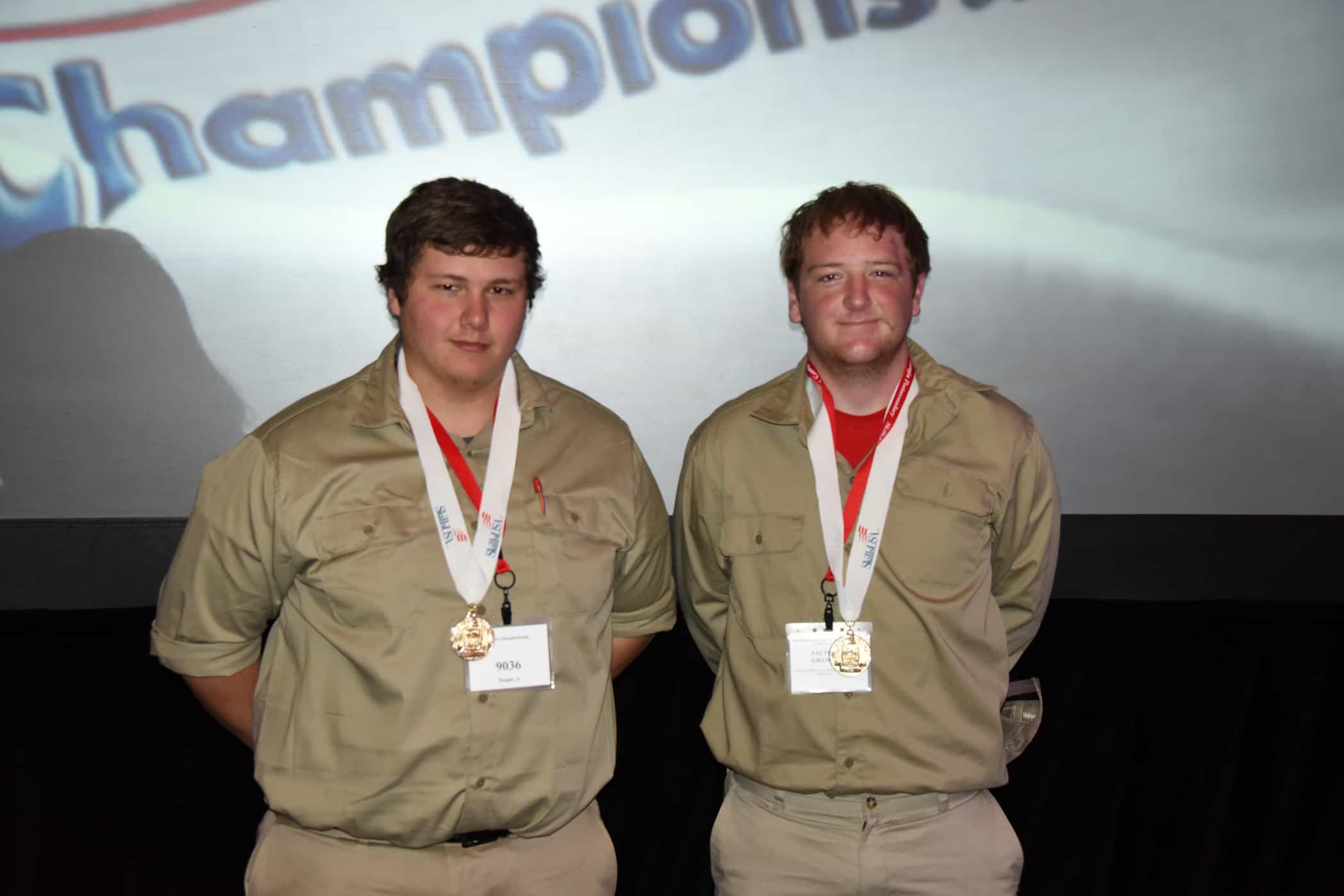 Two males stand together with gold medals around their necks