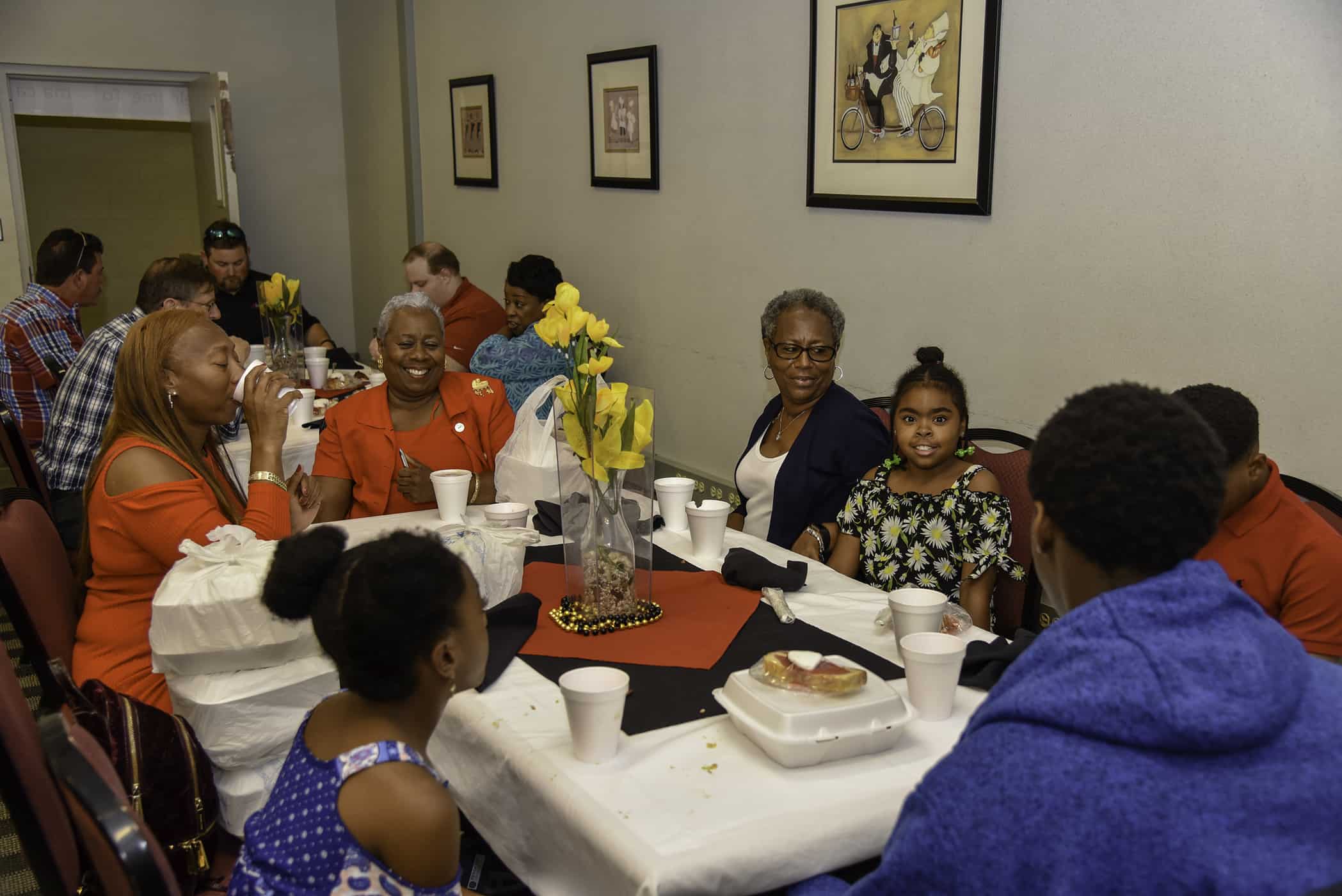 Seven people sit around a table, some smiling, some facing away from the camera.