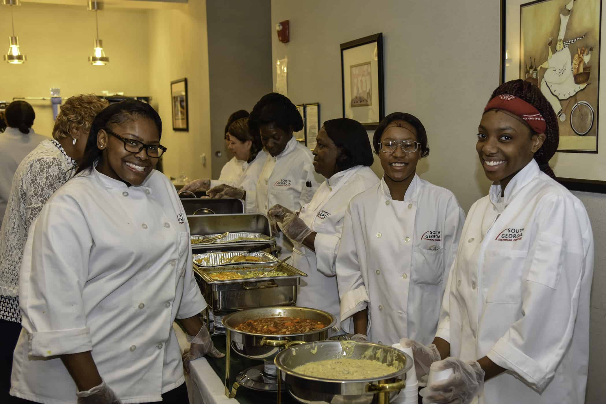 Three females in chef's robes smile.