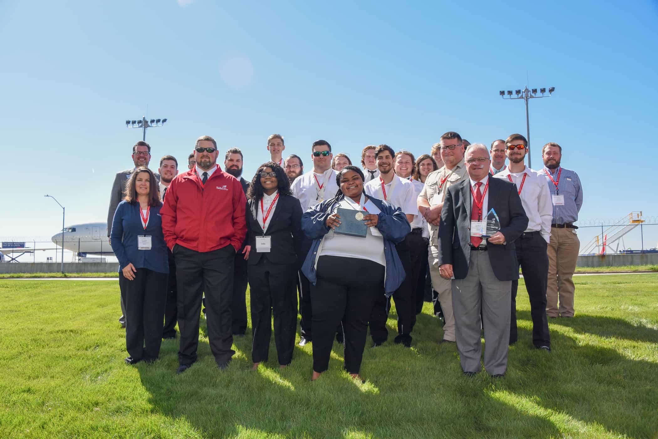 23 people stand in front of a Delta airplane.