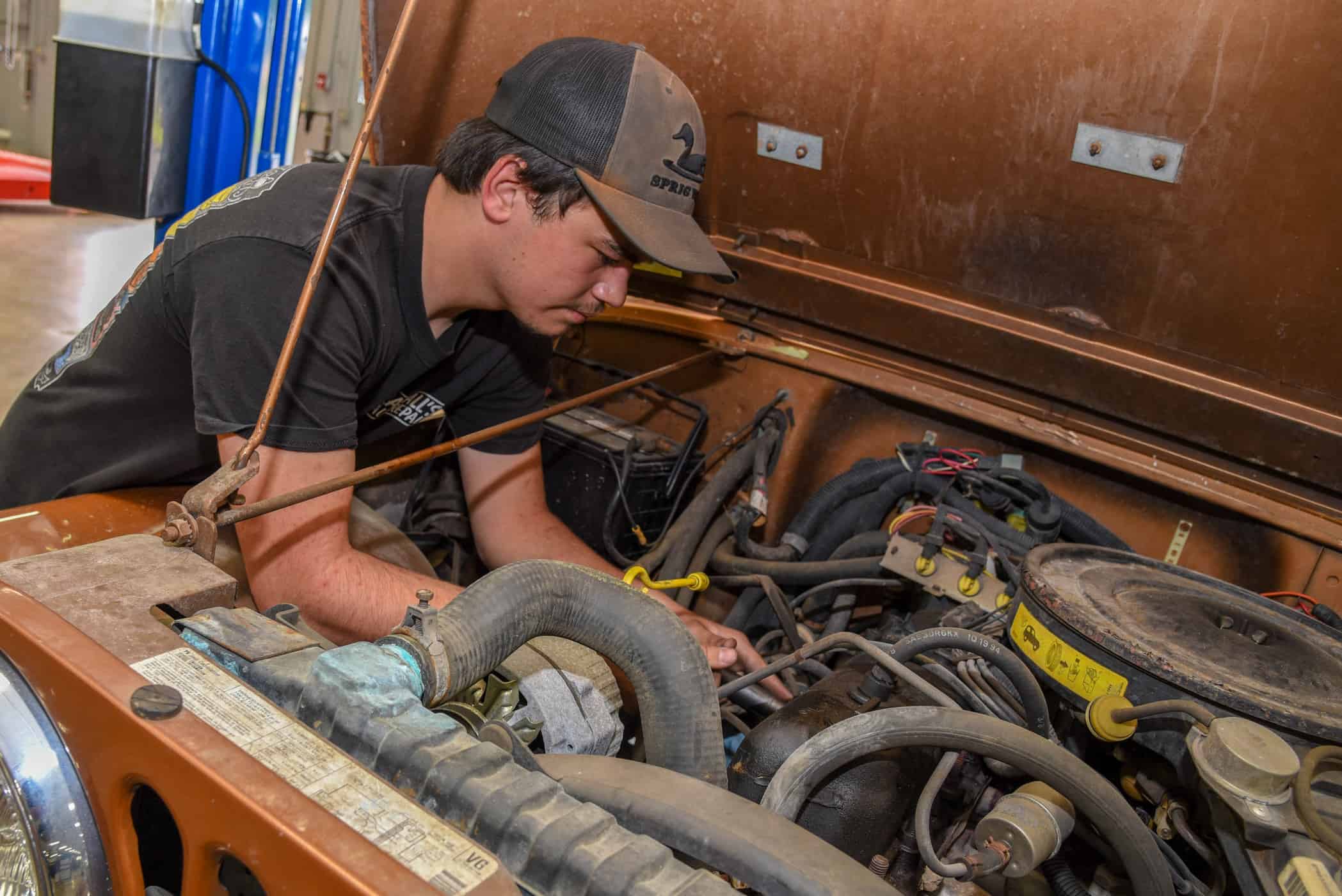 Christopher Waller works under the hood of an burnt orange jeep