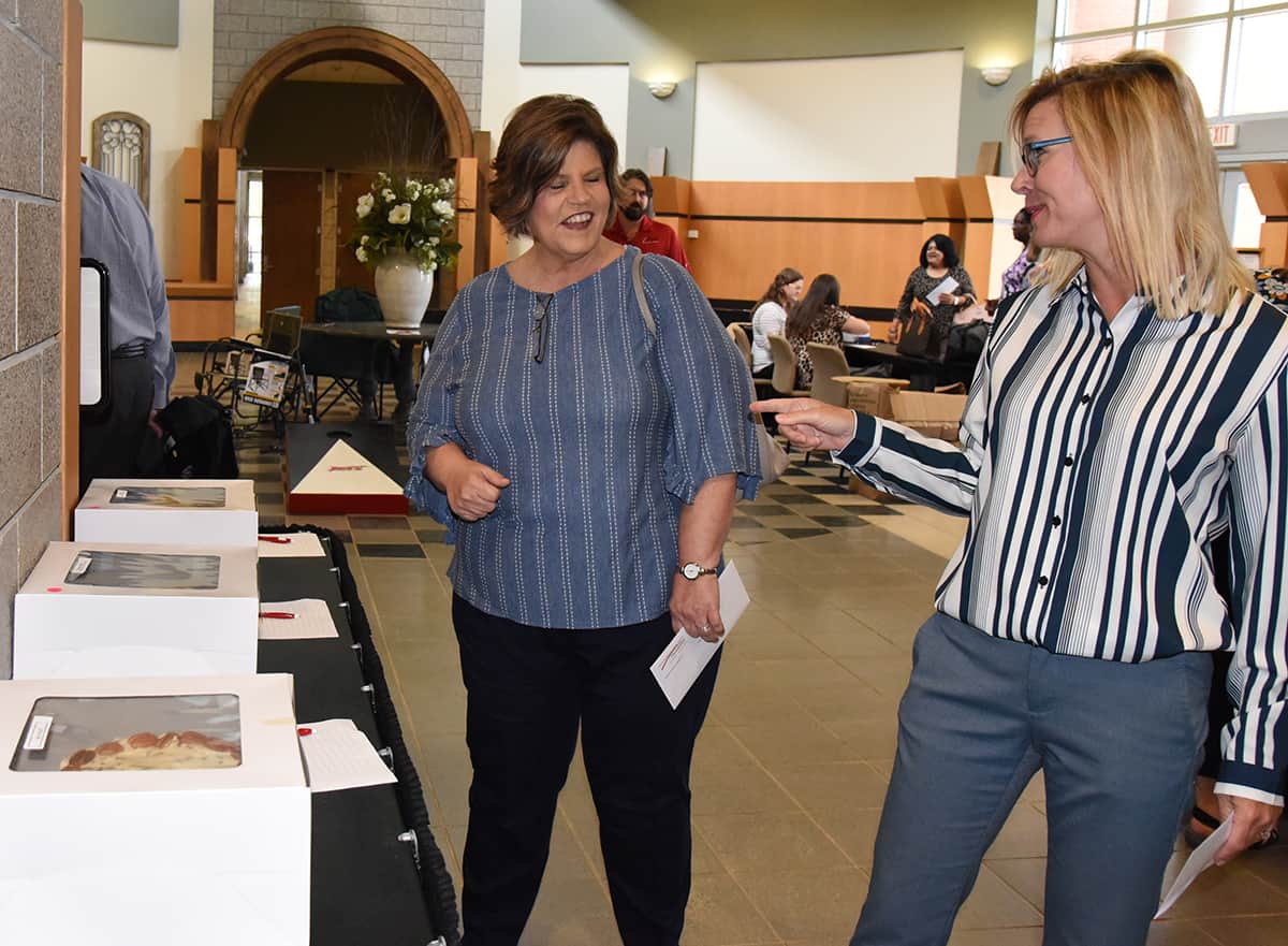 SGTC employees Carol Cowan and Julie Partain are shown above bidding against each other on some of the cakes prepared by the culinary arts students during the silent auction.